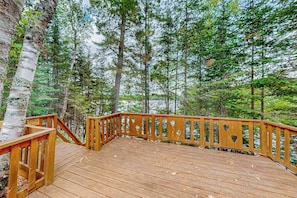 A wooden deck with a railing, surrounded by trees and a body of water.