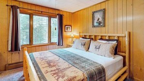 Ein Zimmer mit Holzwänden, einem Bett, einem Deckenventilator und einem Fenster mit Vorhängen.