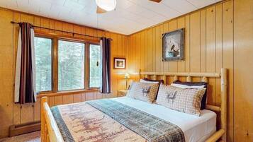 A wooden-paneled room with a bed, a ceiling fan, and a window with curtains.
