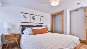 Un dormitorio con cama, mesitas de noche de madera, una lámpara de noche e impresiones botánicas enmarcadas en la pared.