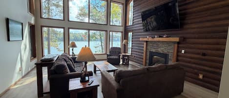 Una sala de estar amplia con chimenea, ventanas grandes y un televisor montado en la pared.