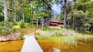Un pontile in legno che conduce a un edificio circondato da alberi e da uno specchio d'acqua.