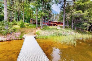 A wooden deck leading to a building surrounded by trees and a body of water.