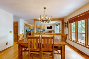 Un comedor con mesa y sillas de madera, una araña y una cocina al fondo.