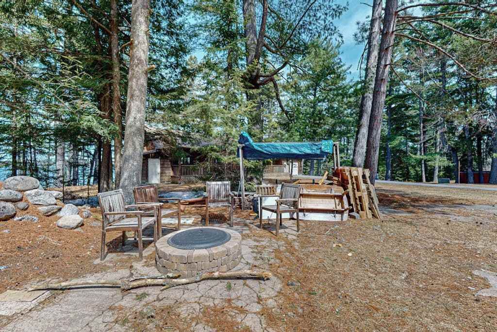 A rustic outdoor seating area with stone fire pit, wooden chairs, and a blue canopy.