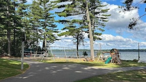 En park med en lekplats, en promenadstig och en sjö i bakgrunden.