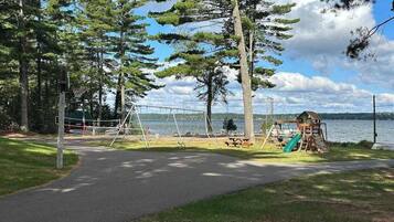 A park with a playground, a walking path, and a lake in the background.