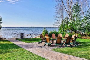 A lakeside patio with Adirondack chairs and a table, a stone pathway, and a view of the lake.