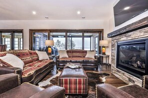 A spacious living room with leather sofas, a stone fireplace, and large windows.