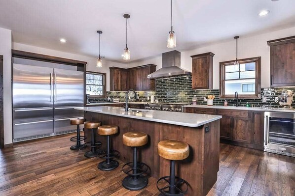 A modern kitchen with a large island, stainless steel appliances, wooden cabinets, and hanging pendant lights.