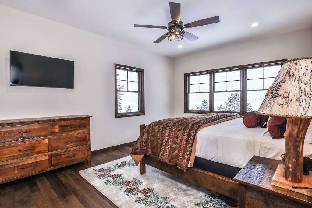 Quarto com cama, penteadeira, janelas e ventoinha no teto.