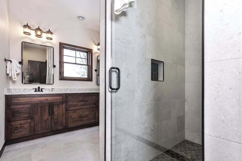 A bathroom with a glass-enclosed shower, a vanity with a mirror, and a window.