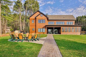 A two-story wooden house with a garage, surrounded by a grassy yard and tall trees.