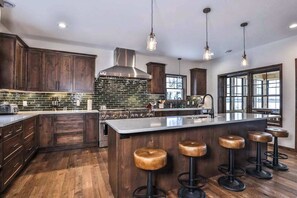 A kitchen with wooden cabinets, a stainless steel range hood, a large island with stools, and pendant lighting.
