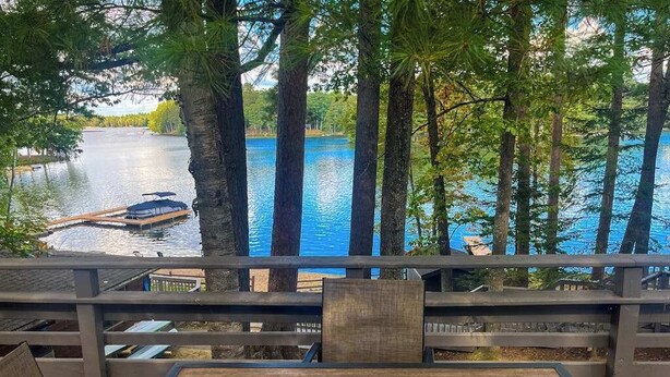 Eine Holzterrasse mit Tisch und Stühlen mit Blick auf einen stillen See und ein Boot.