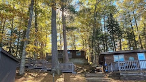 Eine Holzhütte mit einer Holzterrasse, einer Treppe zu einer Veranda und einem bewaldeten Hintergrund.