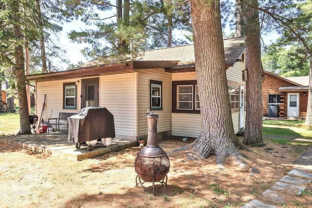 Une cabane en rondins avec une cheminée, un barbecue et un grand arbre devant.