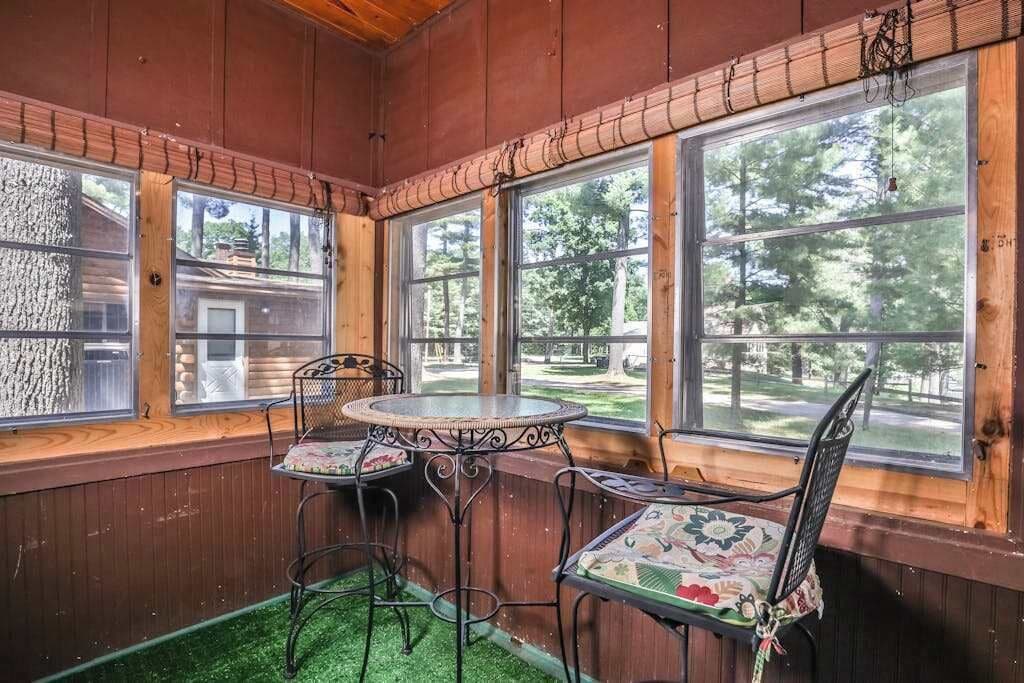 Interior de una cabaña de madera con ventanas amplias, una mesa redonda y dos sillas.