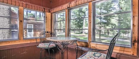 Interior de una cabaña de madera con ventanas amplias, una mesa redonda y dos sillas.