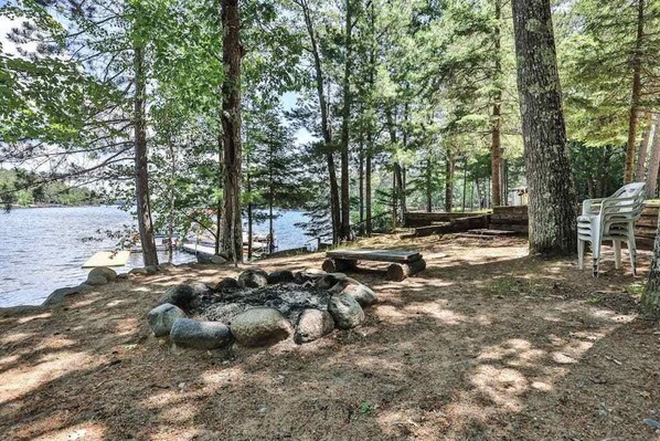 A lakeside campsite with a fire pit, seating area, and chairs. - Lake view, dog-friendly cabin with porch & shared dock, swimming area, firepit (St. Germain)