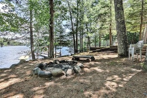 Un camping junto al lago con un brasero, zona de estar y sillas.