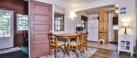 A dining area with a wooden table and chairs, a kitchen with cabinets and appliances, and a door leading to another room.