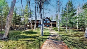 A wooden pathway leading to a cabin surrounded by trees. - Dog-friendly lodging w/ scenic deck, pool table, lake dock, & free WiFi (St. Germain)