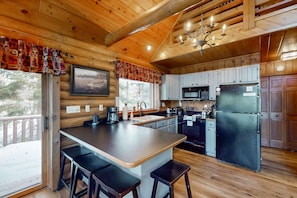A wooden cabin interior with a kitchen, bar stools, a refrigerator, and a dining area. - Spacious and beautiful lakefront log home on 7 acres with private dock (Presque Isle)
