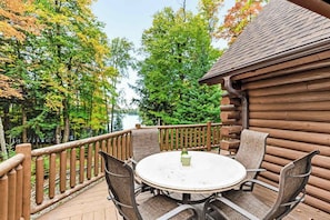 A wooden deck with a round table and chairs, surrounded by a wooden railing, overlooking a forested area. - Spacious and beautiful lakefront log home on 7 acres with private dock (Presque Isle)
