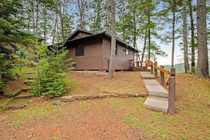 A cabin with a wooden exterior, a concrete staircase, and a small tree in front.