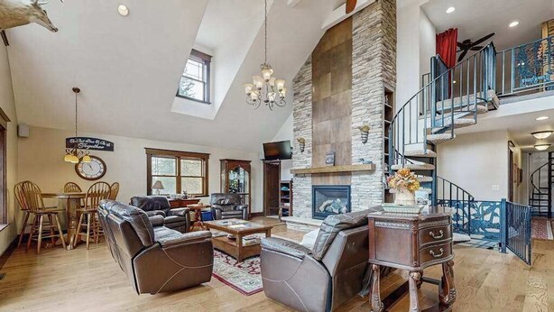 A spacious living room with a stone fireplace, leather sofas, a dining area with wooden furniture, and a staircase leading to an upper level. - Large, waterfront home w/ a full kitchen, dock, canoes, & outdoor firepit (Tomahawk)