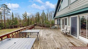 A wooden deck with a table and chairs, surrounded by a forest. - Large, waterfront home w/ a full kitchen, dock, canoes, & outdoor firepit (Tomahawk)