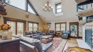 A spacious living room with leather sofas, a chandelier, a fireplace, and large windows. - Large, waterfront home w/ a full kitchen, dock, canoes, & outdoor firepit (Tomahawk)