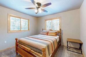 Ein Schlafzimmer mit einem hölzernen Bett, Deckenventilator, zwei Fenstern und einem kleinen Tisch.