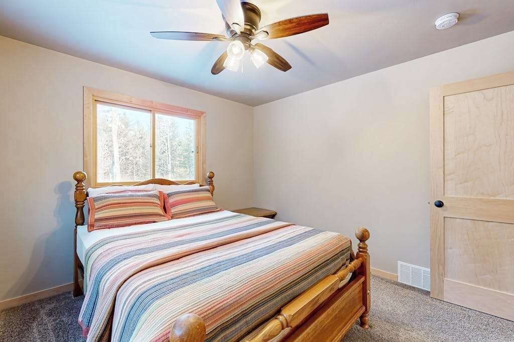 A bedroom with a bed, a ceiling fan, a window, and a door.
