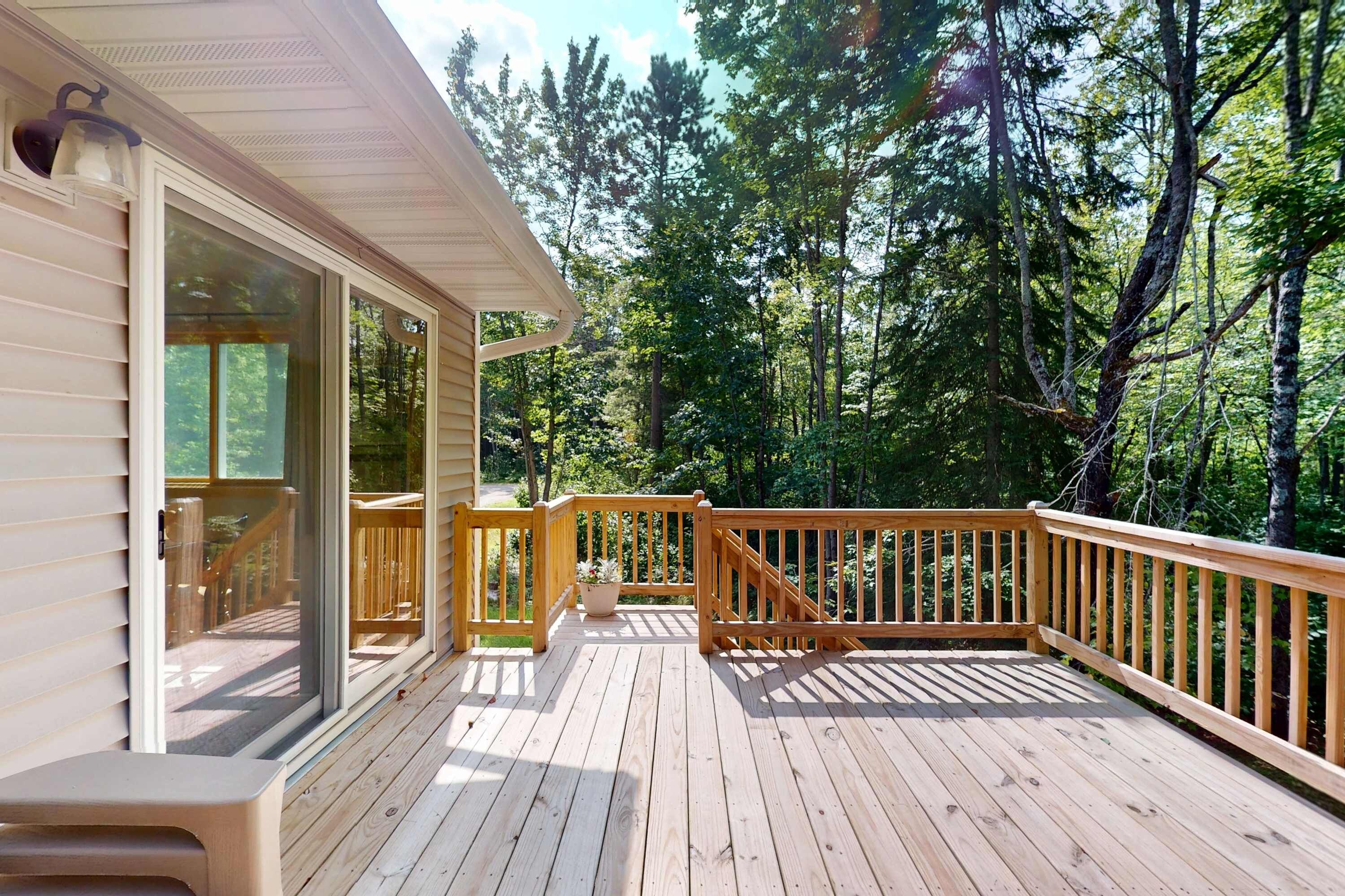 A wooden deck with a railing, overlooking a forested area.