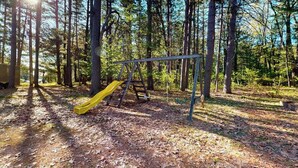 Un parque infantil con un tobogán amarillo y columpios metálicos en un área boscosa.