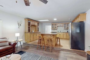 A modern kitchen with wooden cabinets, a black refrigerator, and a central island with stools. - Dog-friendly, tree-lined home on the snowmobile trail with streaming, W/D, & AC (Manitowish Waters)