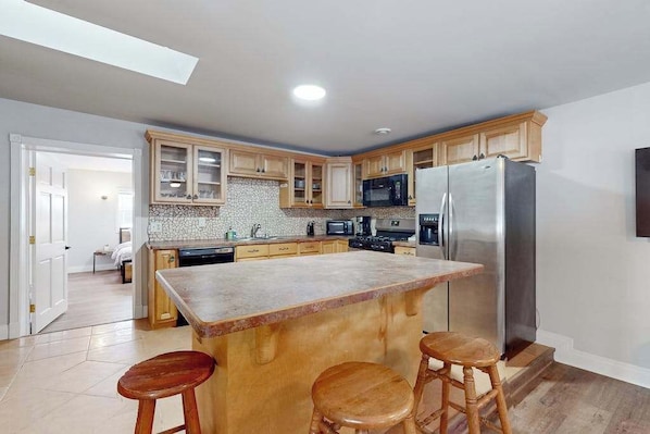 A kitchen with wooden cabinets, a large island with stools, a stainless steel refrigerator, and a microwave. - Dog-friendly, tree-lined home on the snowmobile trail with streaming, W/D, & AC (Manitowish Waters)