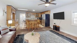 Une cuisine moderne avec des meubles en bois, un îlot central doté de tabourets, un grand réfrigérateur et un ventilateur de plafond.