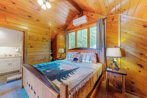 A wooden cabin bedroom with a bed, bedside lamps, a window, and a ceiling fan.