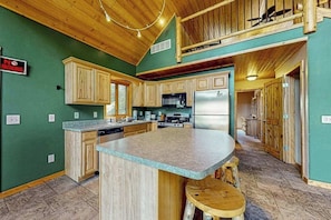 A kitchen with wooden cabinets, a central island, and a dining area with stools. - Cozy Home located on the Turtle Flambeau Flowage, great for all seasons! (Mercer)