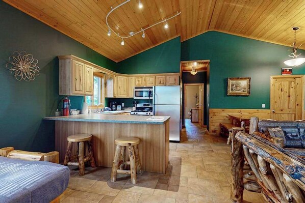 A kitchen with wooden cabinets, a central island with stools, and a dining area with a wooden bench. - Cozy Cabin on the Turtle Flambeau Flowage, great for all seasons! (Mercer)
