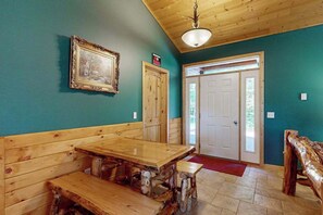 A room with a wooden bench seating area, a table, a framed picture on the wall, and a door leading outside.