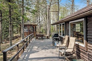 A wooden deck with outdoor furniture and a gazebo in a forested area.