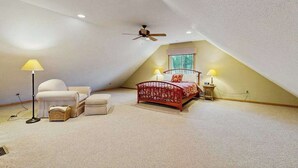 Een slaapkamer met een schuine kap, een bed, twee bedlampjes, een vloerlamp en een plafondventilator.