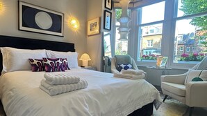 Ein modernes Schlafzimmer mit einem großen Bett, einem Sessel, einem Fenster mit Blick und einer Lampe.