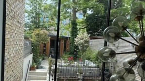 Ein Zimmer mit großem Fenster, einer Treppe und Blick auf einen Garten sowie Gebäude.