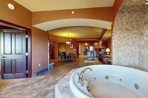 A spacious bathroom with a large bathtub, a wooden door, and a tiled wall. - Wisconsin Dells Escape | Adventure Perks Included (Wisconsin Dells)