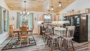Una cocina con armarios de madera, una isla central, taburetes de bar y un refrigerador.
